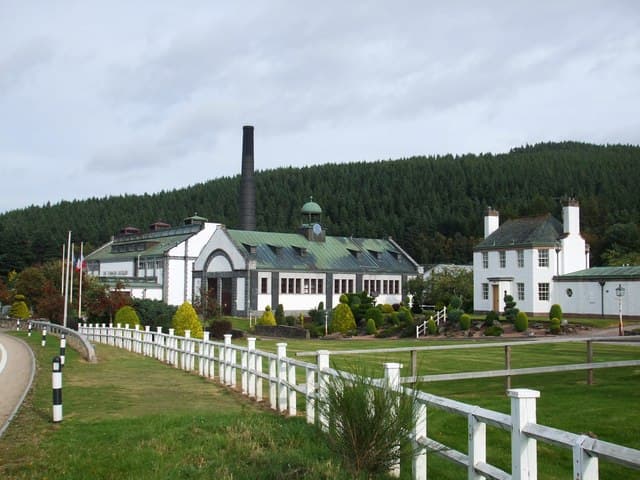 The ornate white frontage and chimney of Tormore distillery below the forested hillside