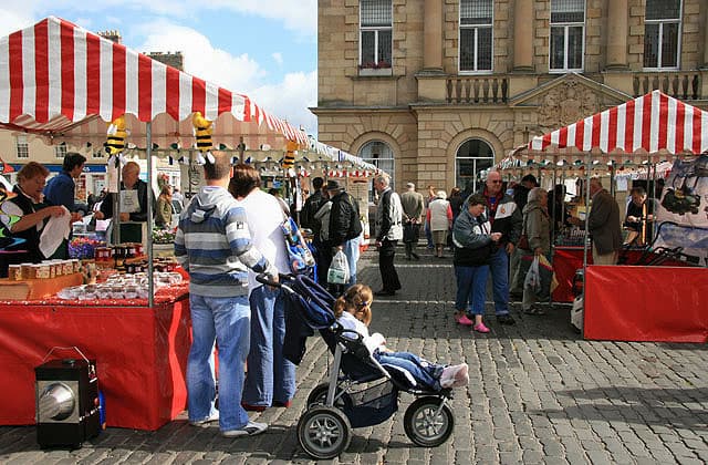 Red and white striped stalls of Kelso Farmers Market in The Square, the town hall behind