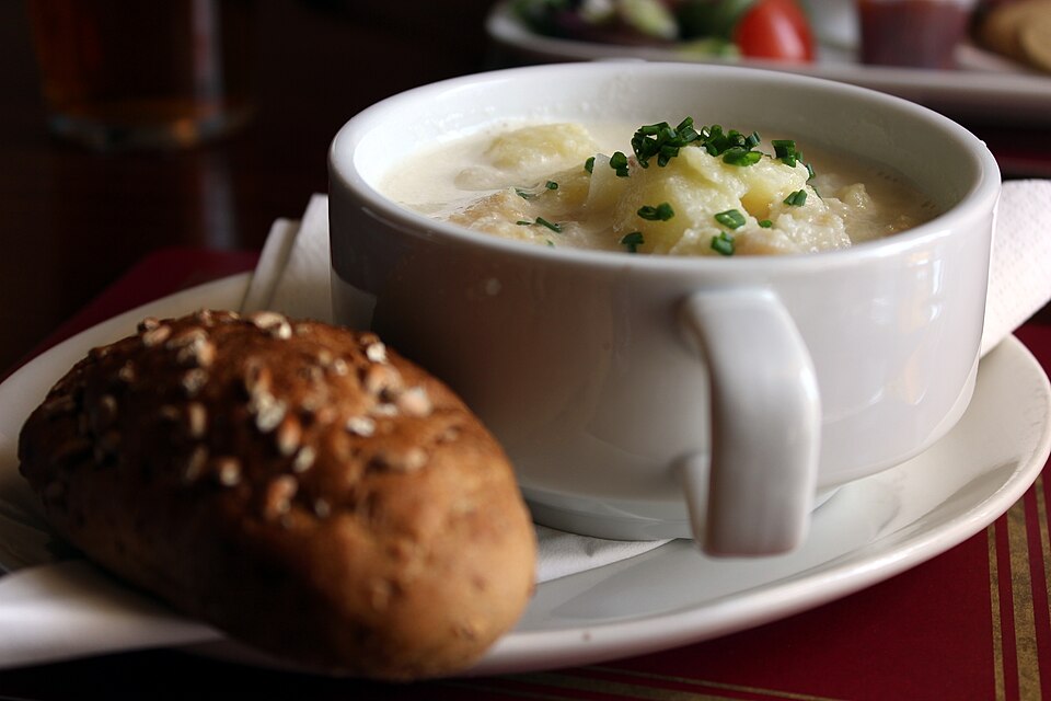 A bowl of cullen skink - creamy smoked haddock and potato soup topped with chives, served with an oat-crusted roll